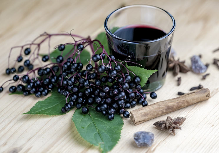 Glass-of-fresh-elderberry-syrup-with-cinnamon-stick-brown-sugar-star-anise-and-elderberries-on-a-wooden-kitchen-counter.jpg